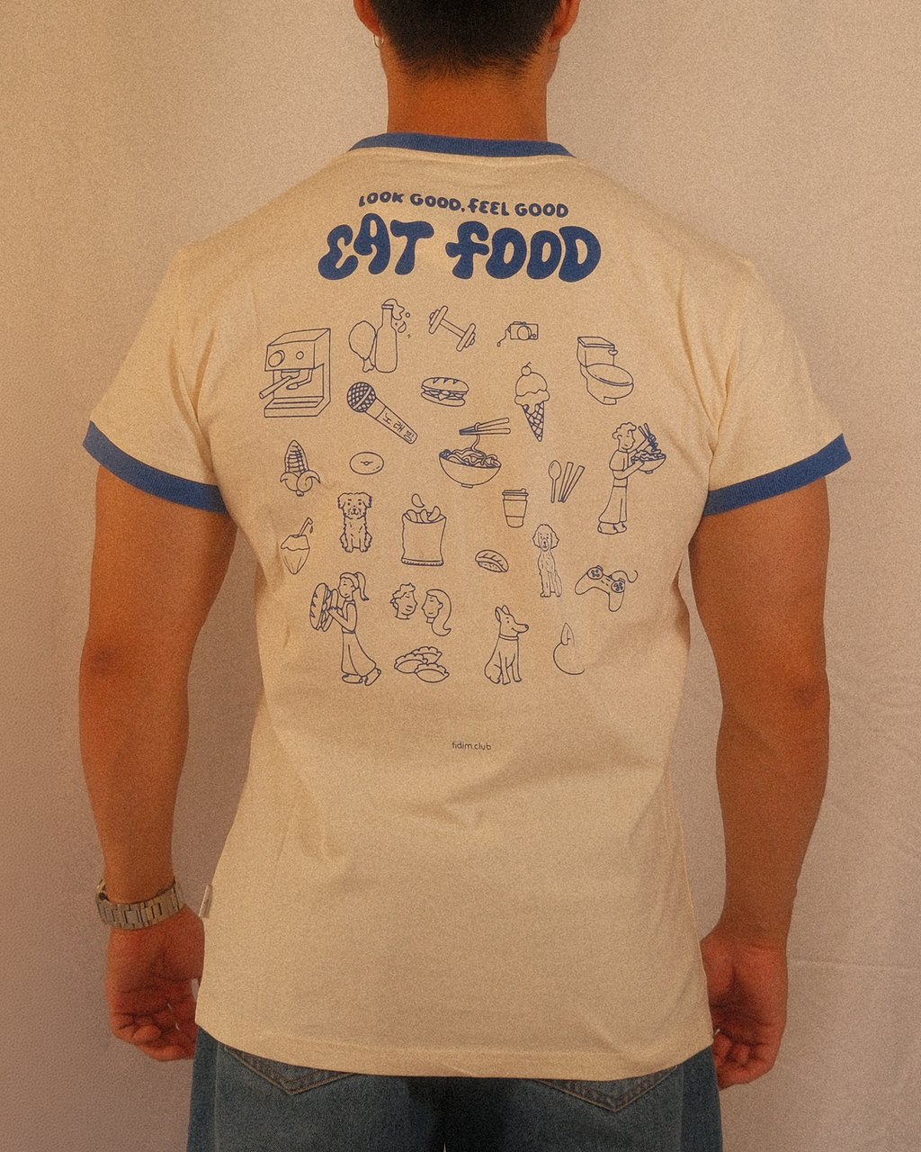 Person wearing a beige regular fit t-shirt with blue text and graphics on the back against a plain background
