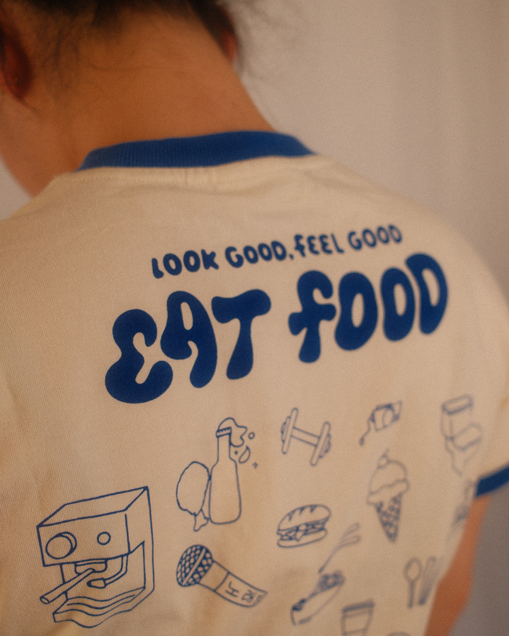 Person wearing a regular fit t-shirt with 'Look Good, Feel Good Eat Food' text and food illustrations.